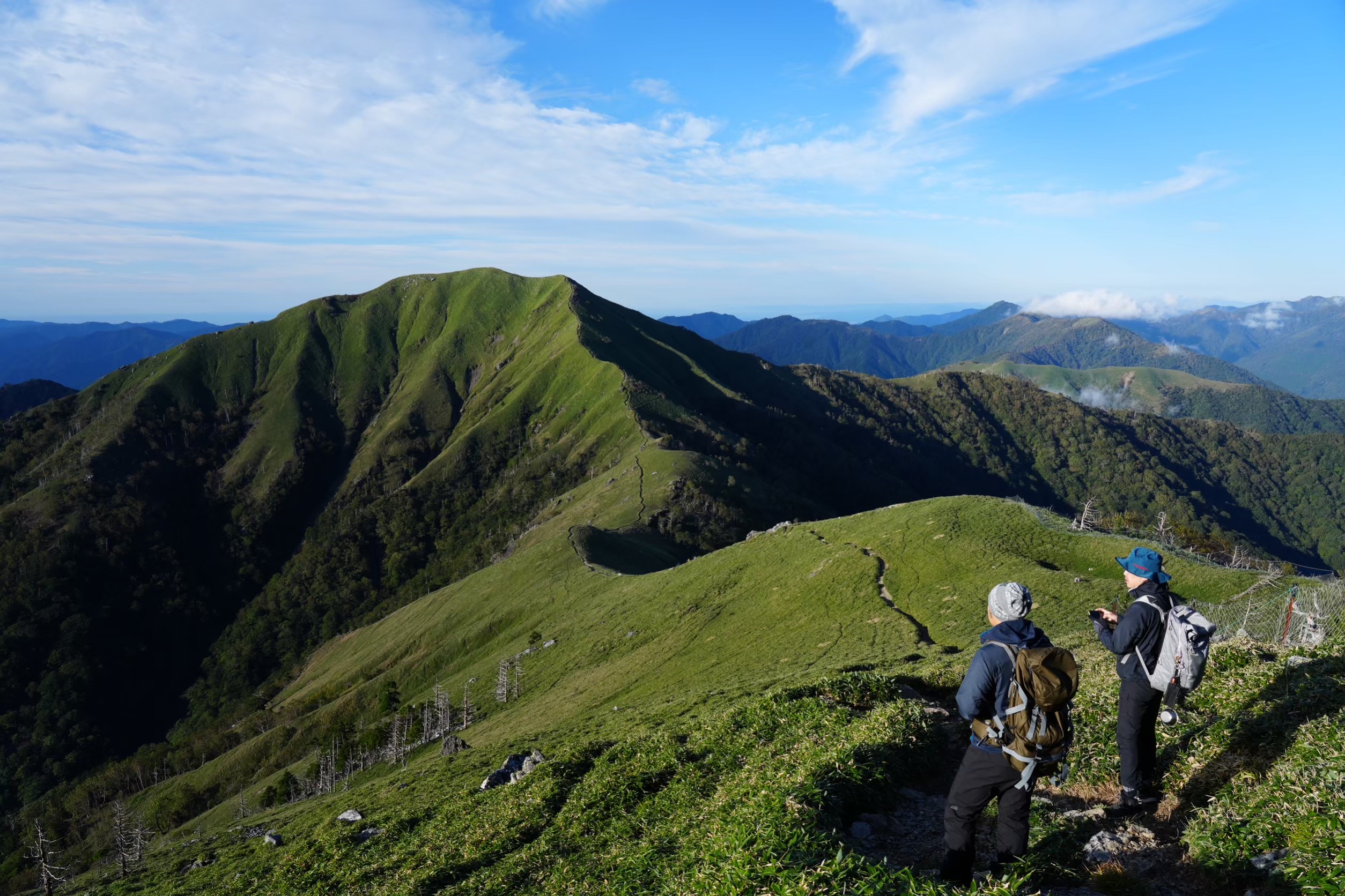 緑の稜線と山並みを眺める登山者